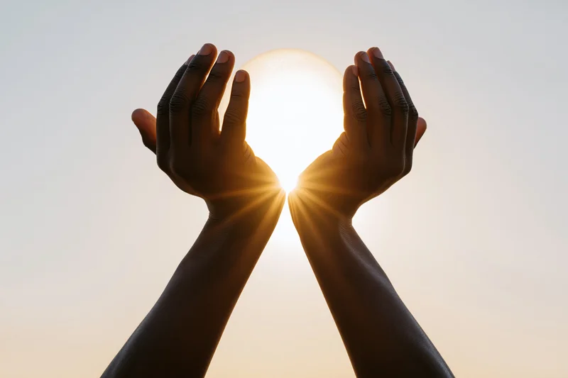 Hands cupping the sun against a glowing sky at sunrise