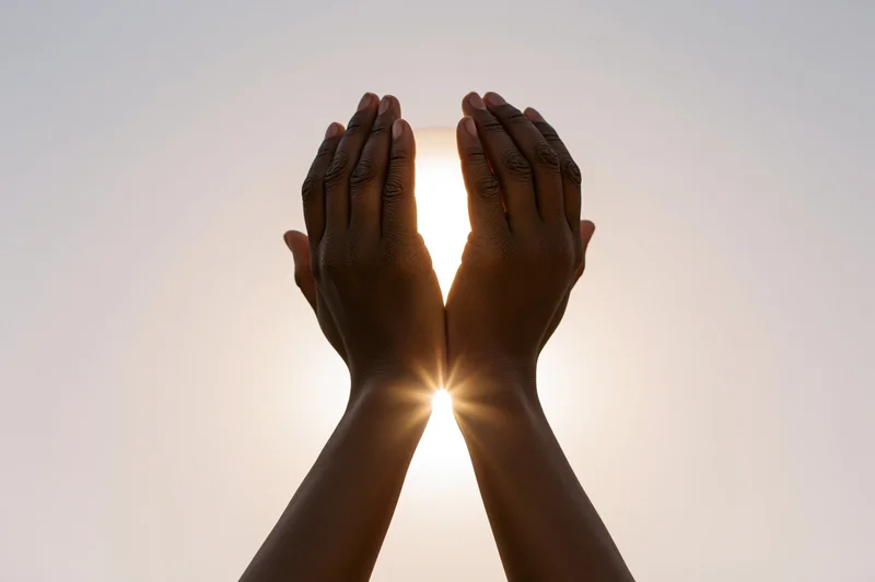 Hands raised upward cupping sunlight against a clear sky