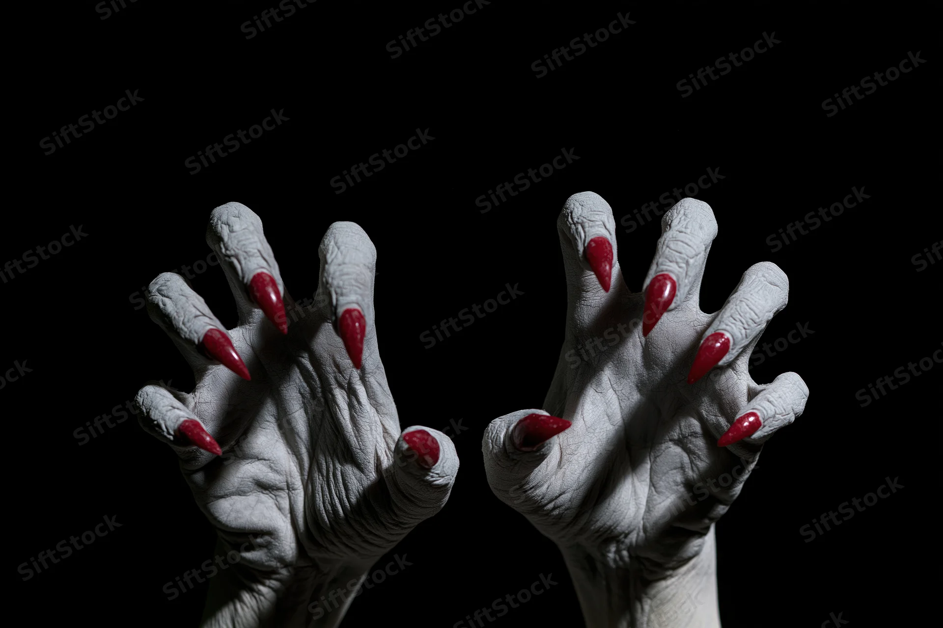 Pale grey clawed hands with red nails reaching forward from darkness