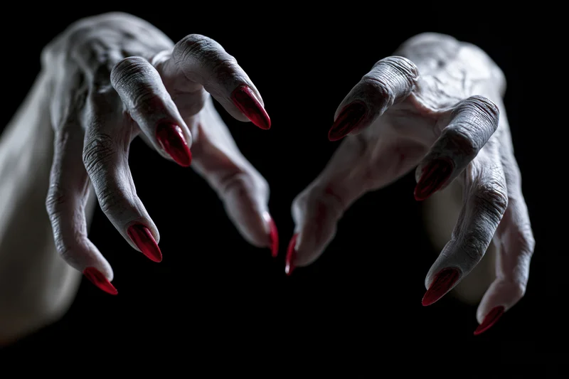 Pale clawed hands with sharp red nails reaching forward against black background