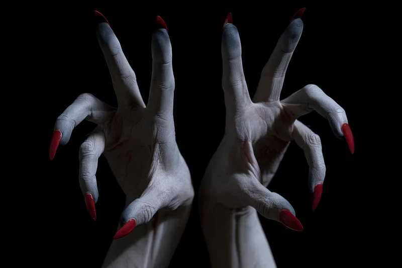Pale grey hands with long red sharp nails reaching forward against black background