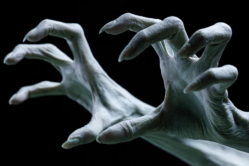 Pale grey contorted hands with long sharp nails reaching against black background