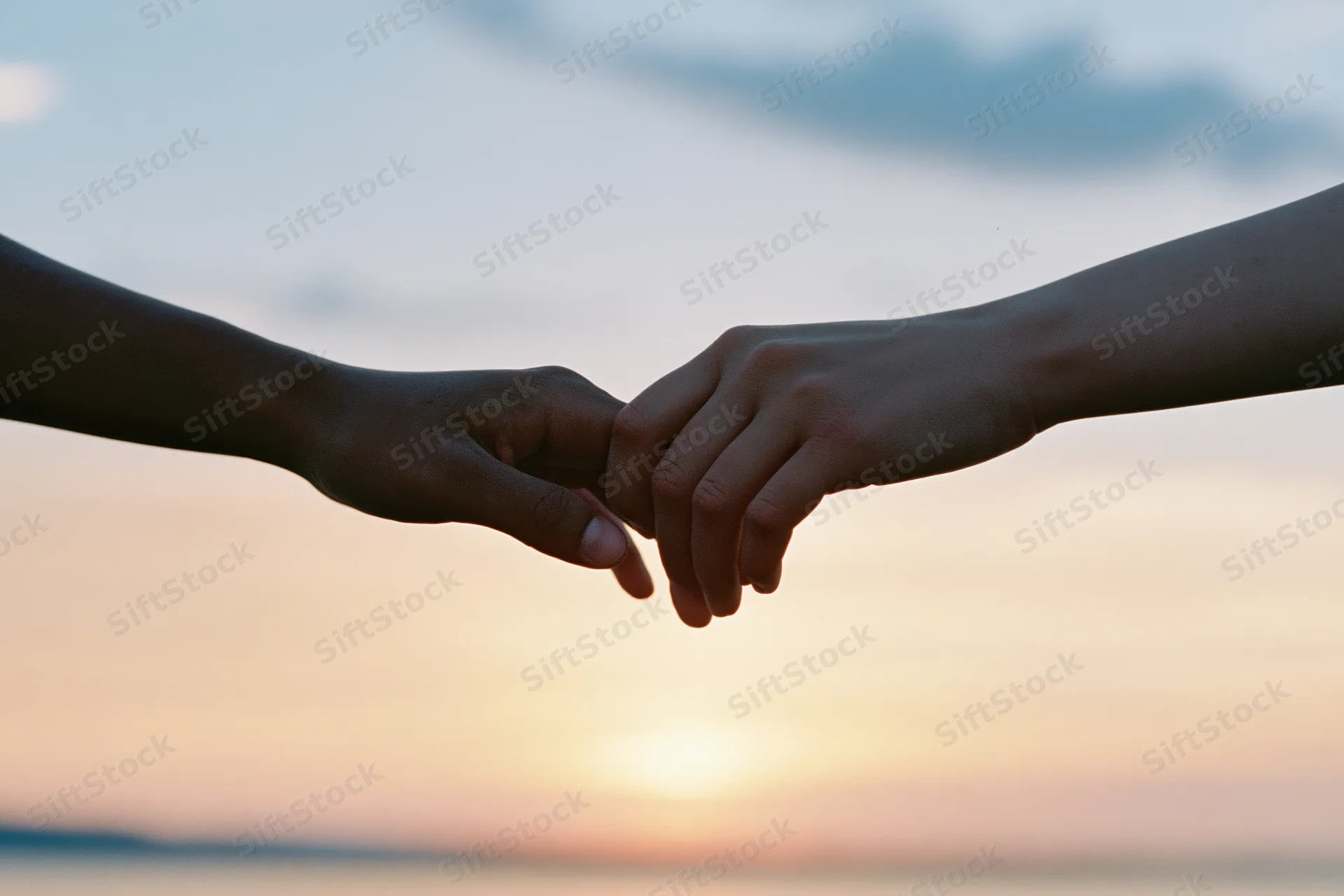 Two people holding hands in silhouette against a sunset sky