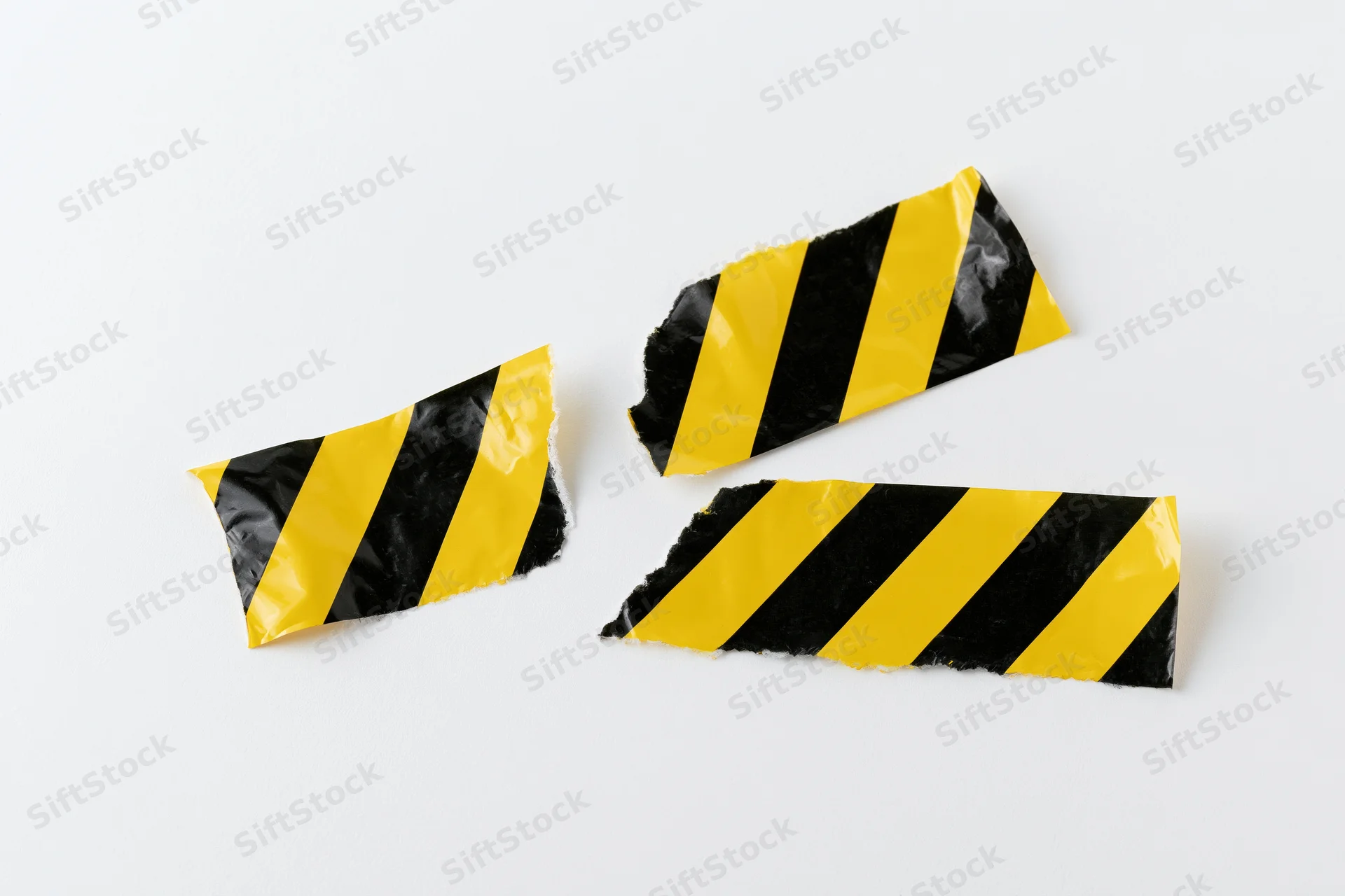 Torn pieces of yellow and black striped hazard tape on white background