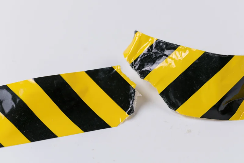 Torn pieces of yellow and black diagonal striped hazard tape on white surface