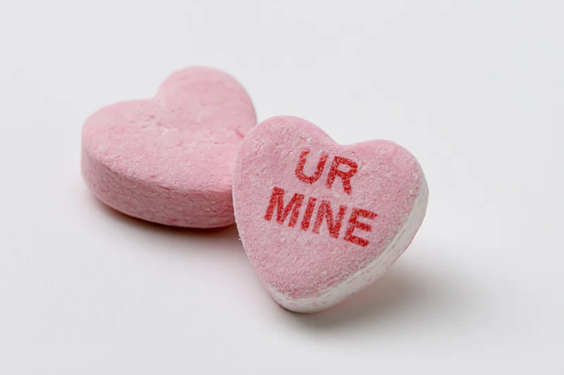 Two pink heart-shaped candies with "UR MINE" text on white background