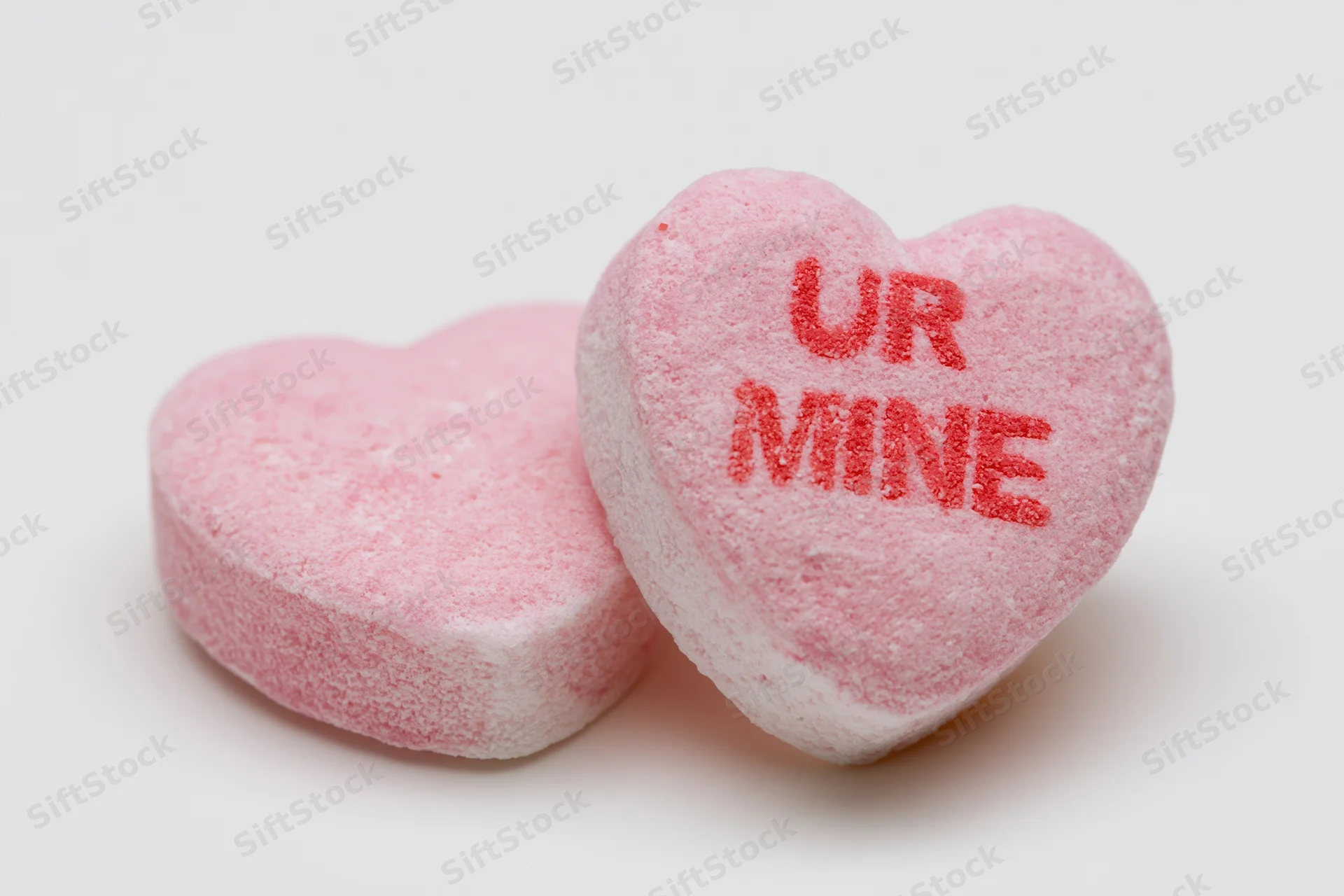 Two pink heart-shaped candies with text ur mine on white background