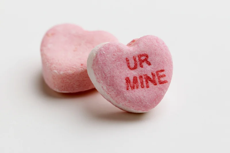 Two pink heart-shaped candies with "ur mine" text on white background