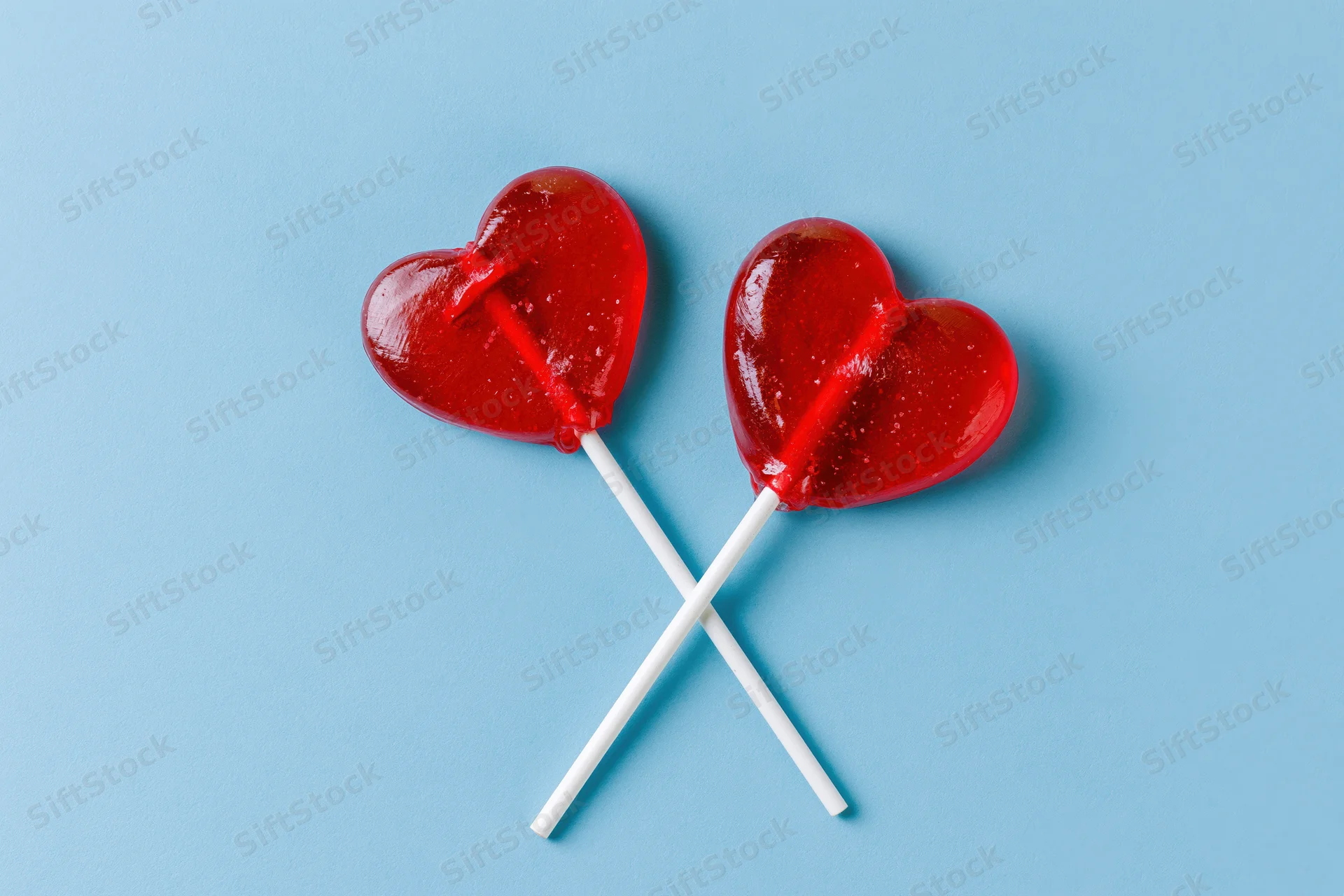 Two red heart-shaped lollipops crossed on a blue background