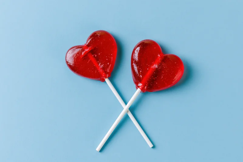 Two red heart-shaped lollipops crossed on a blue background