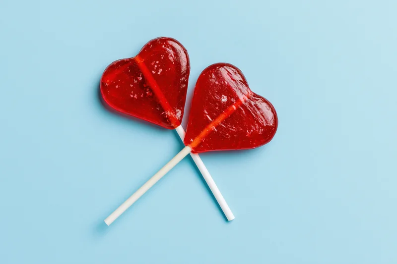 Two red heart-shaped lollipops crossed on a blue background