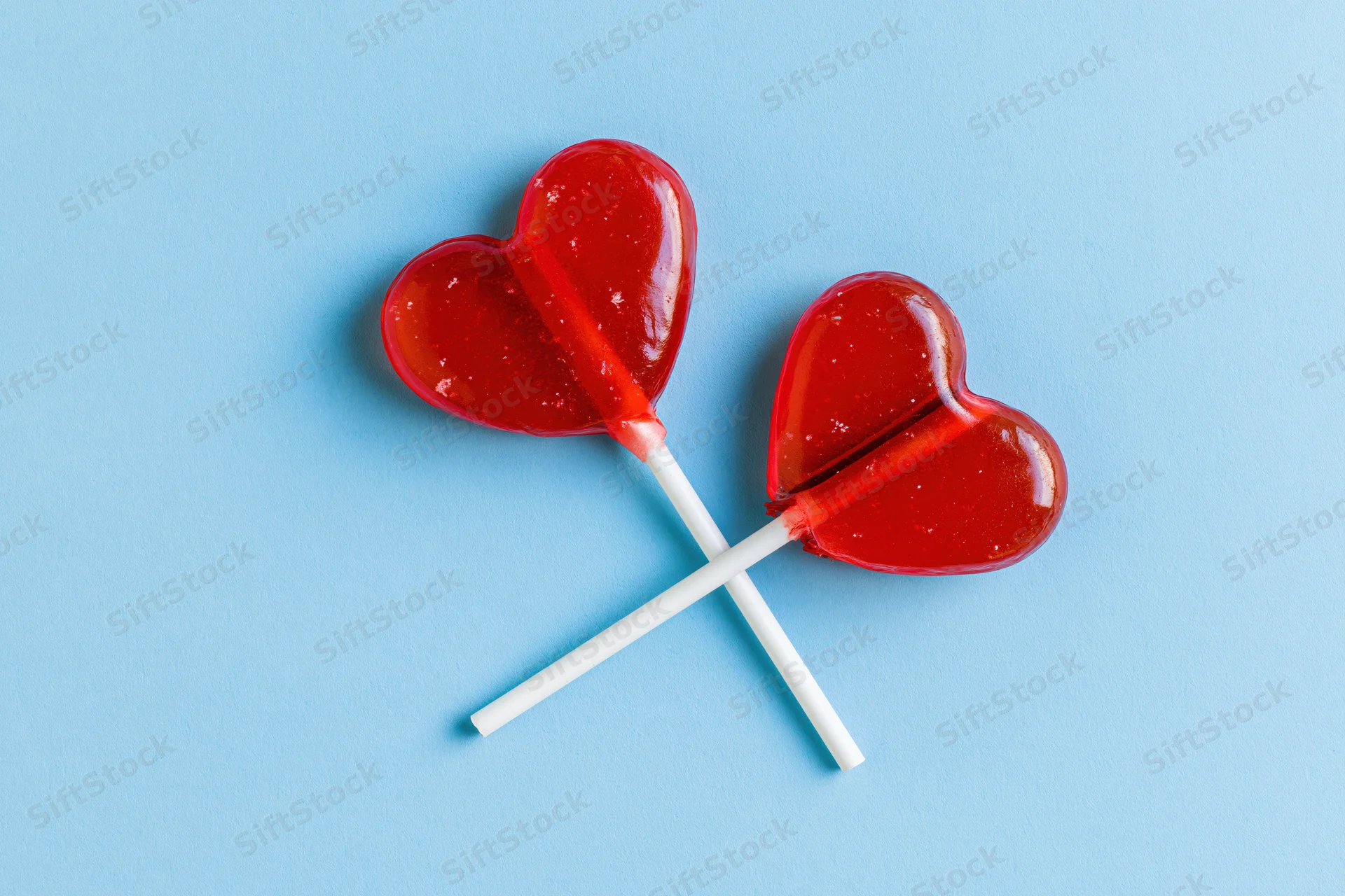 Two red heart-shaped lollipops crossed on a blue background