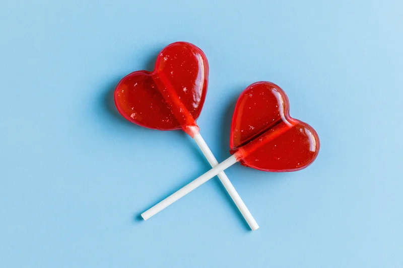 Two red heart-shaped lollipops crossed on a blue background