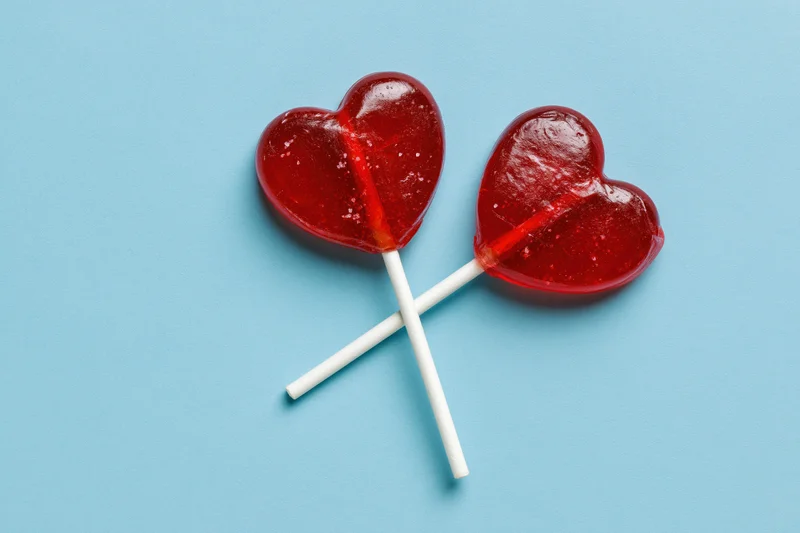 Two red heart-shaped lollipops crossed on a blue background