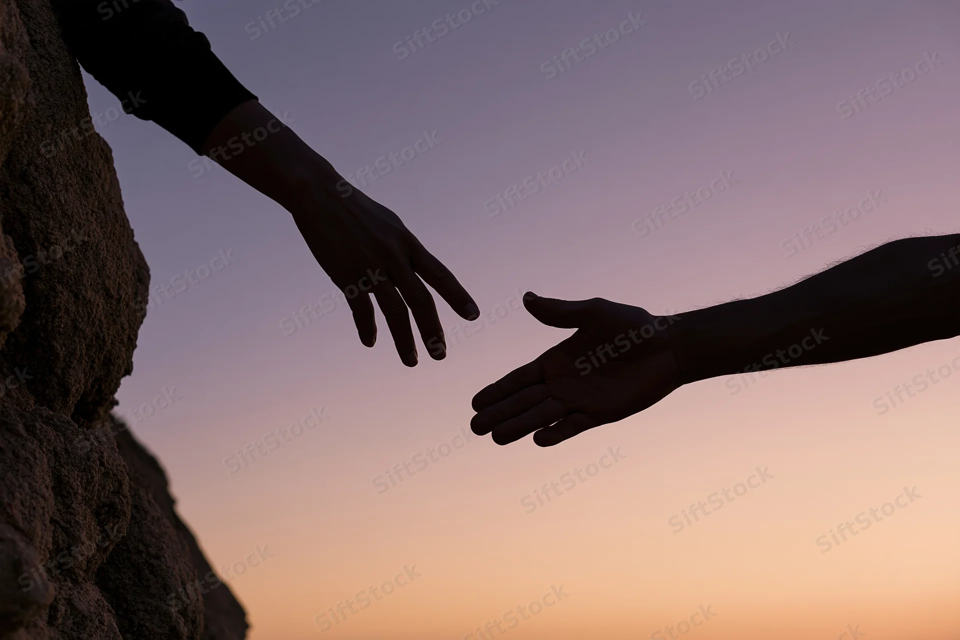 Silhouetted hands reaching toward each other against a twilight sky near a rocky cliff