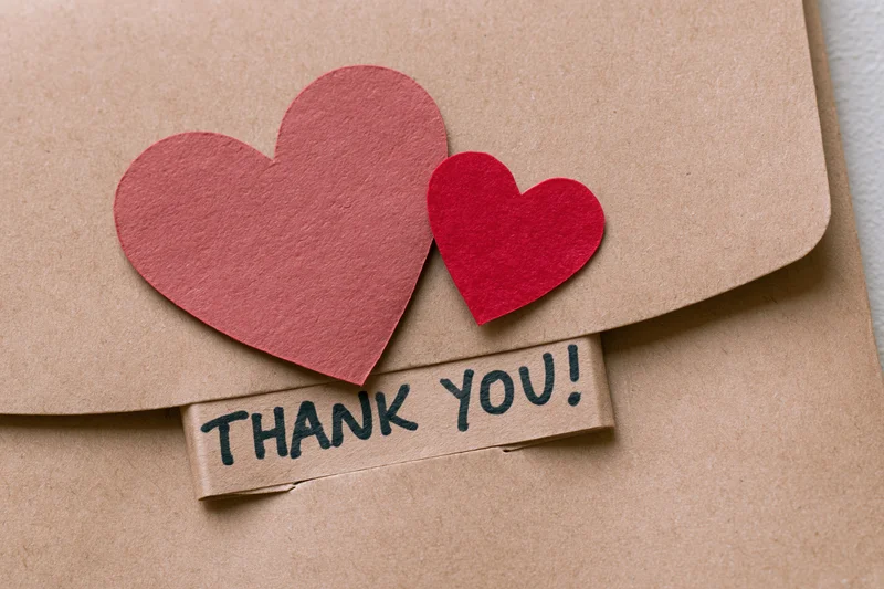 Two red paper hearts on a kraft envelope with a thank you label attached