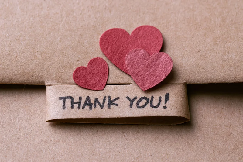 Brown paper-wrapped gift with red paper hearts and thank you tag