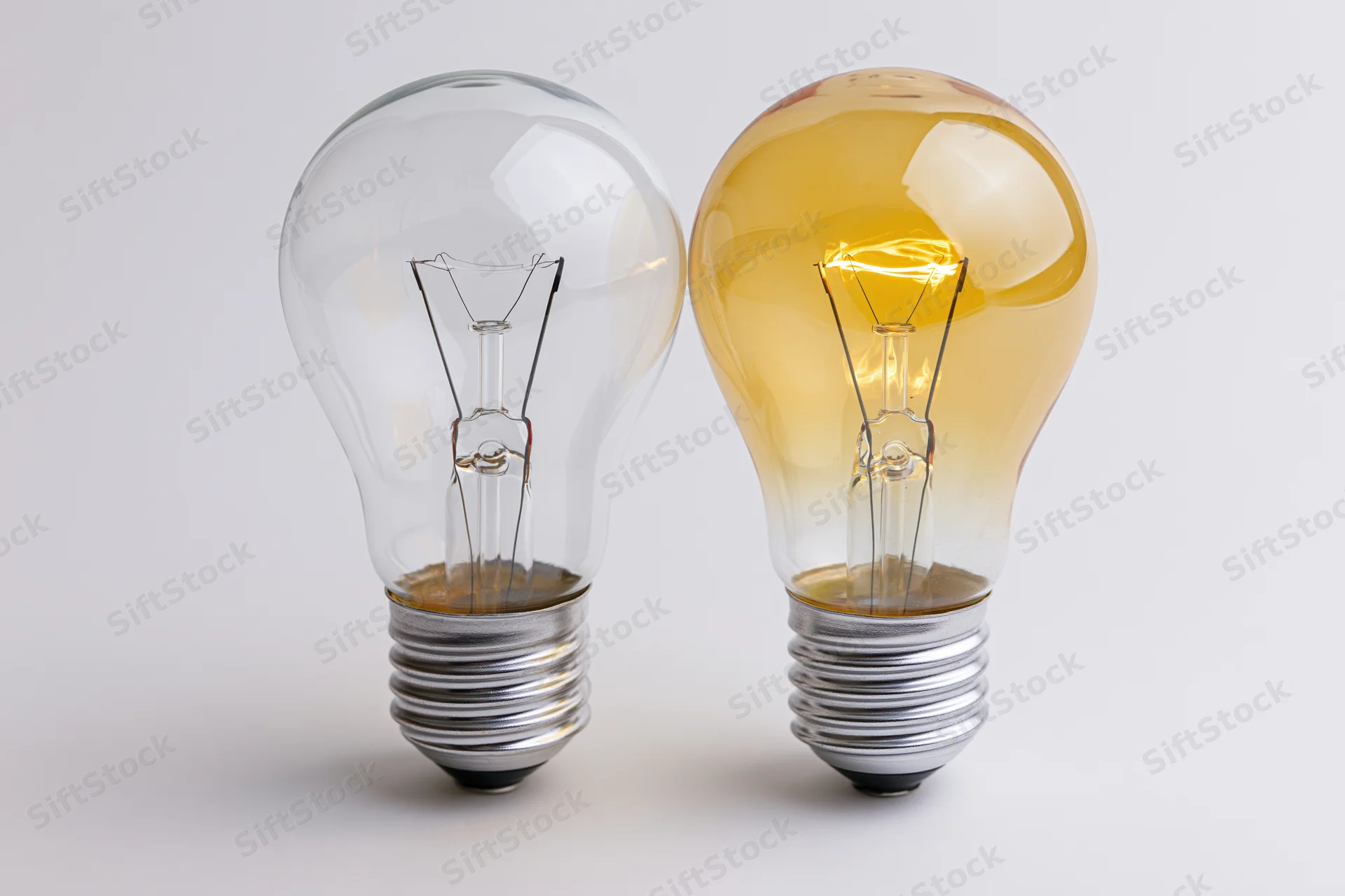 Two incandescent light bulbs side by side, one lit and one unlit, on a plain white surface