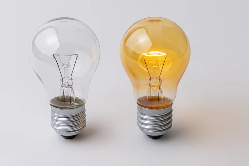 Two incandescent light bulbs side by side on a white surface, one lit and one unlit