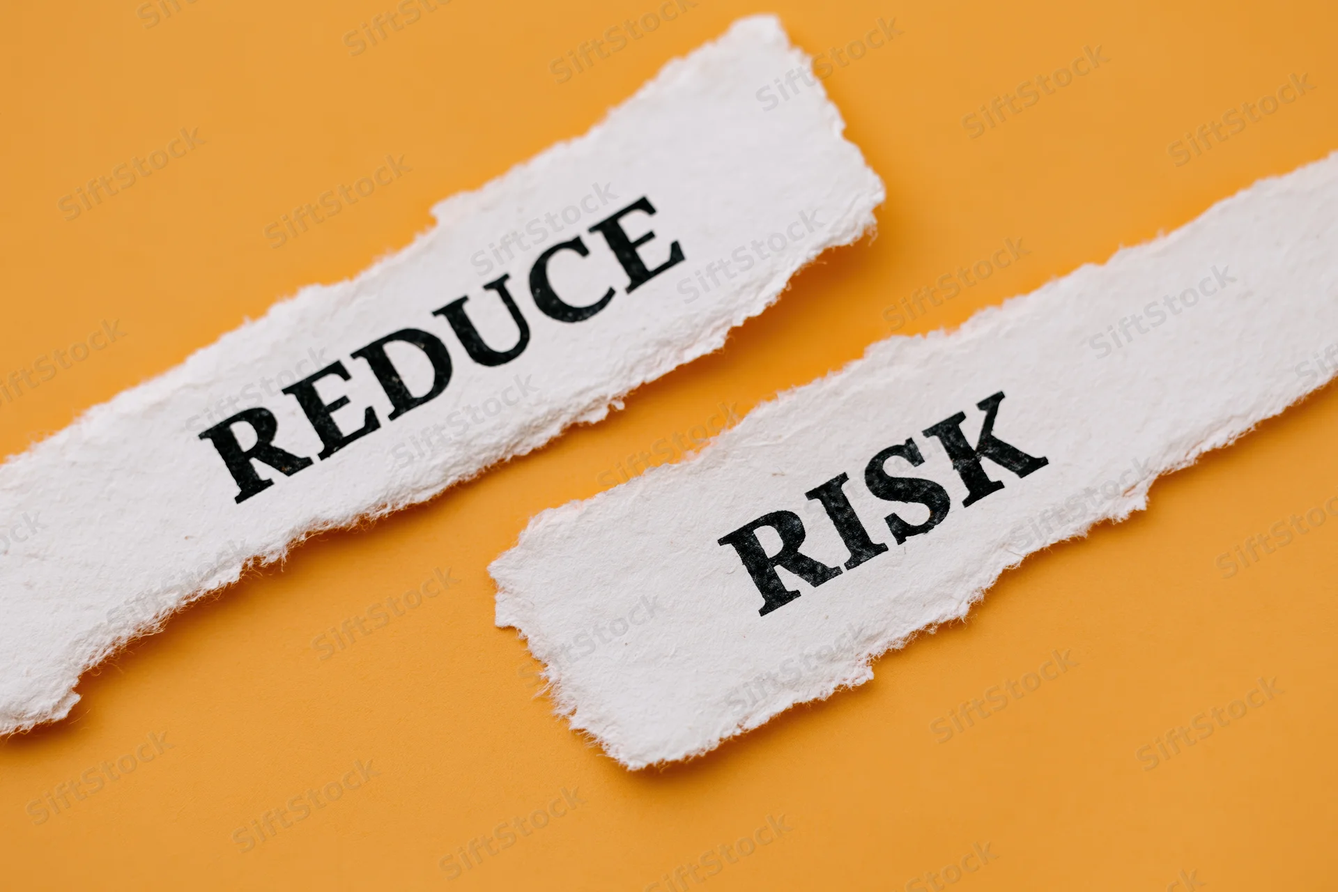 Torn strips of white paper with the words reduce and risk on orange background