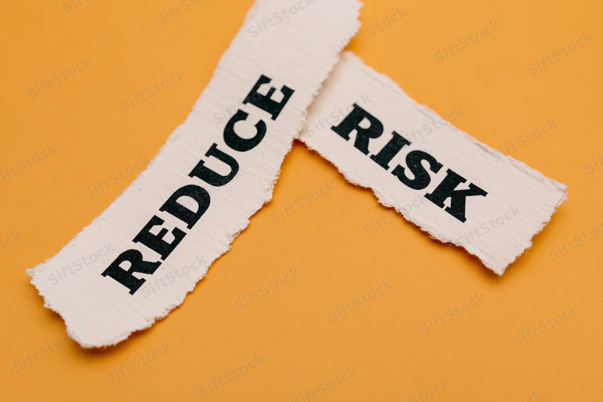 Torn paper strips with the words reduce and risk on orange background