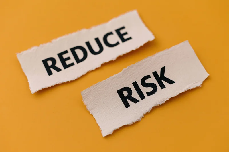 Torn paper strips with the words reduce and risk on an orange background
