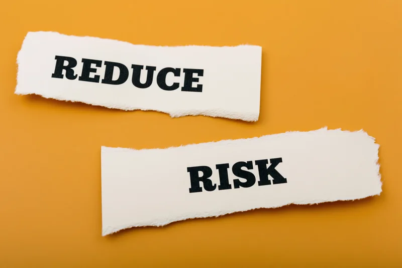 Torn paper strips with the words reduce and risk on orange background