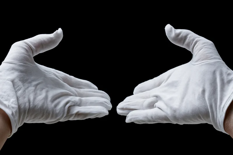 Two white-gloved hands reaching inward from opposite sides against black background