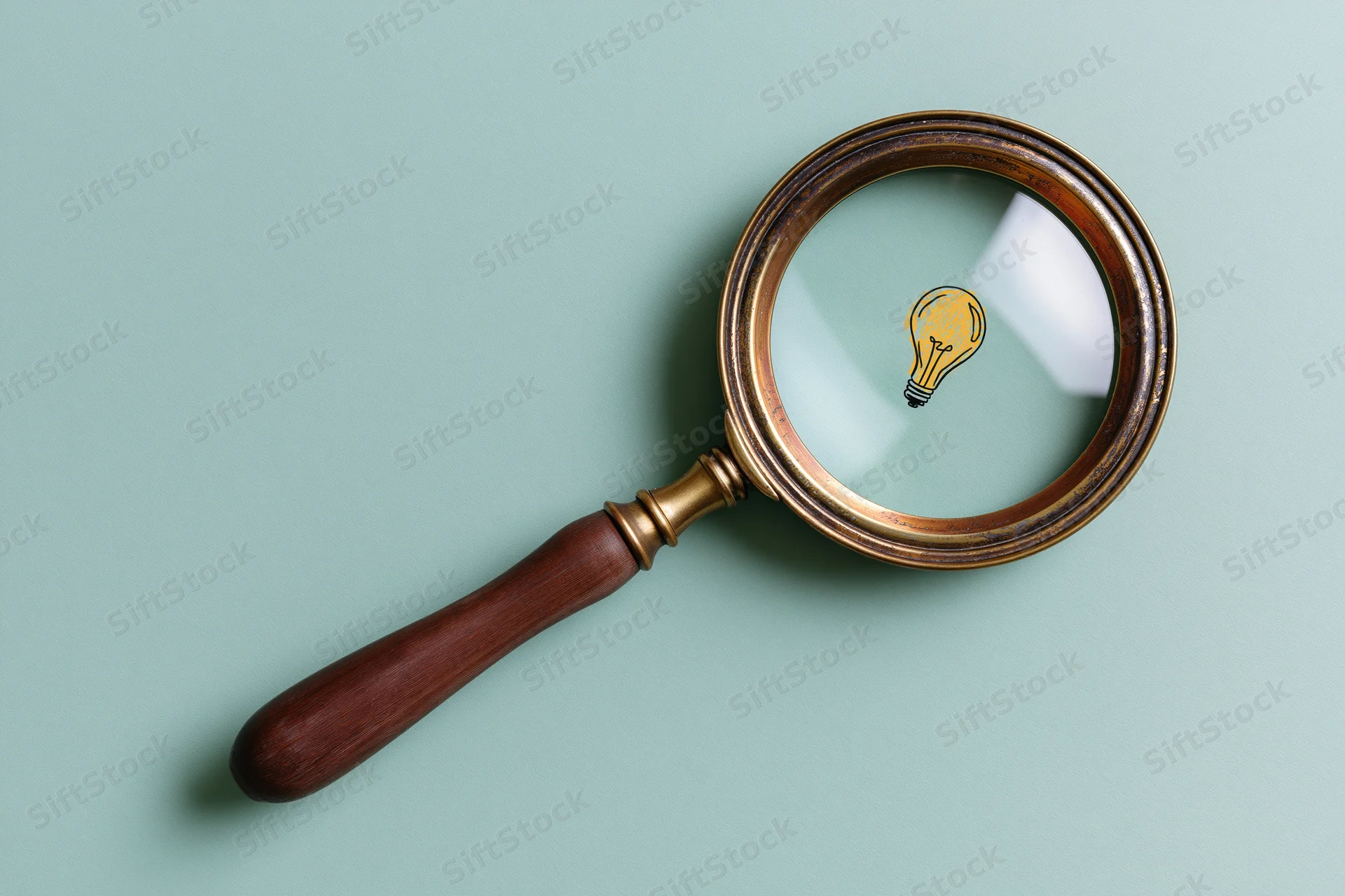 Vintage brass and wood magnifying glass lying flat on mint background with lightbulb symbol visible through lens