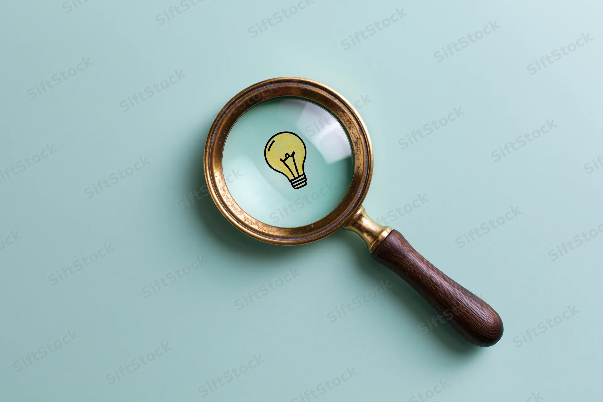 Vintage brass and wood magnifying glass lying flat on mint background with illustrated lightbulb visible through lens