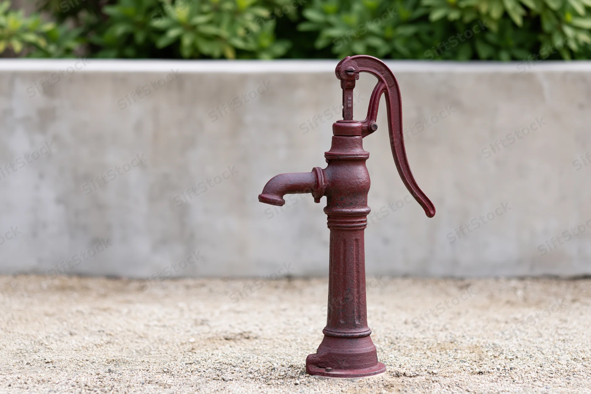 Vintage cast iron hand water pump standing on gravel in a garden setting