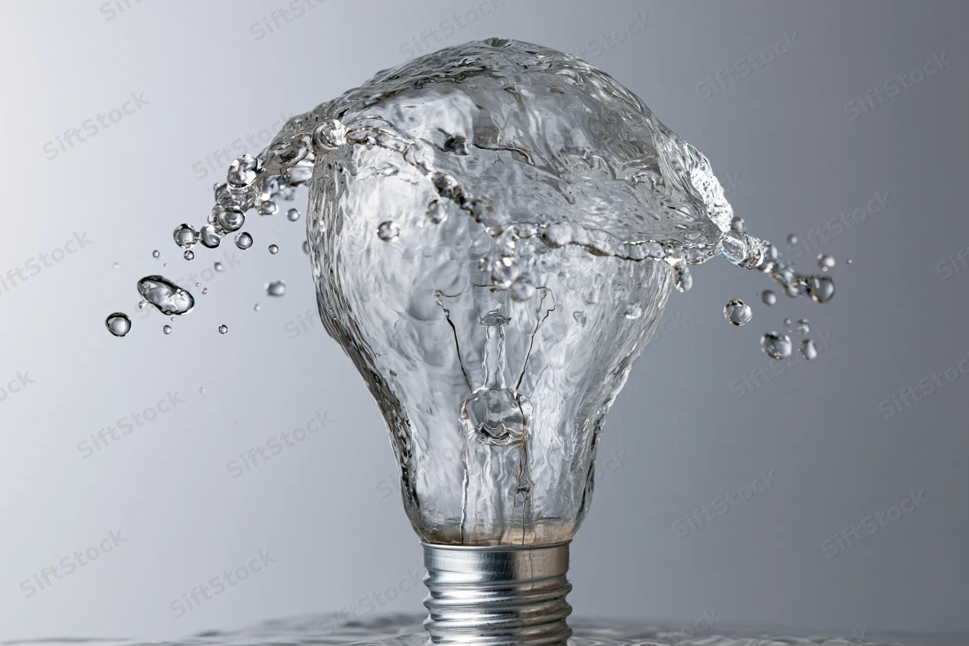 Water splashing in shape of lightbulb frozen midair against gray background