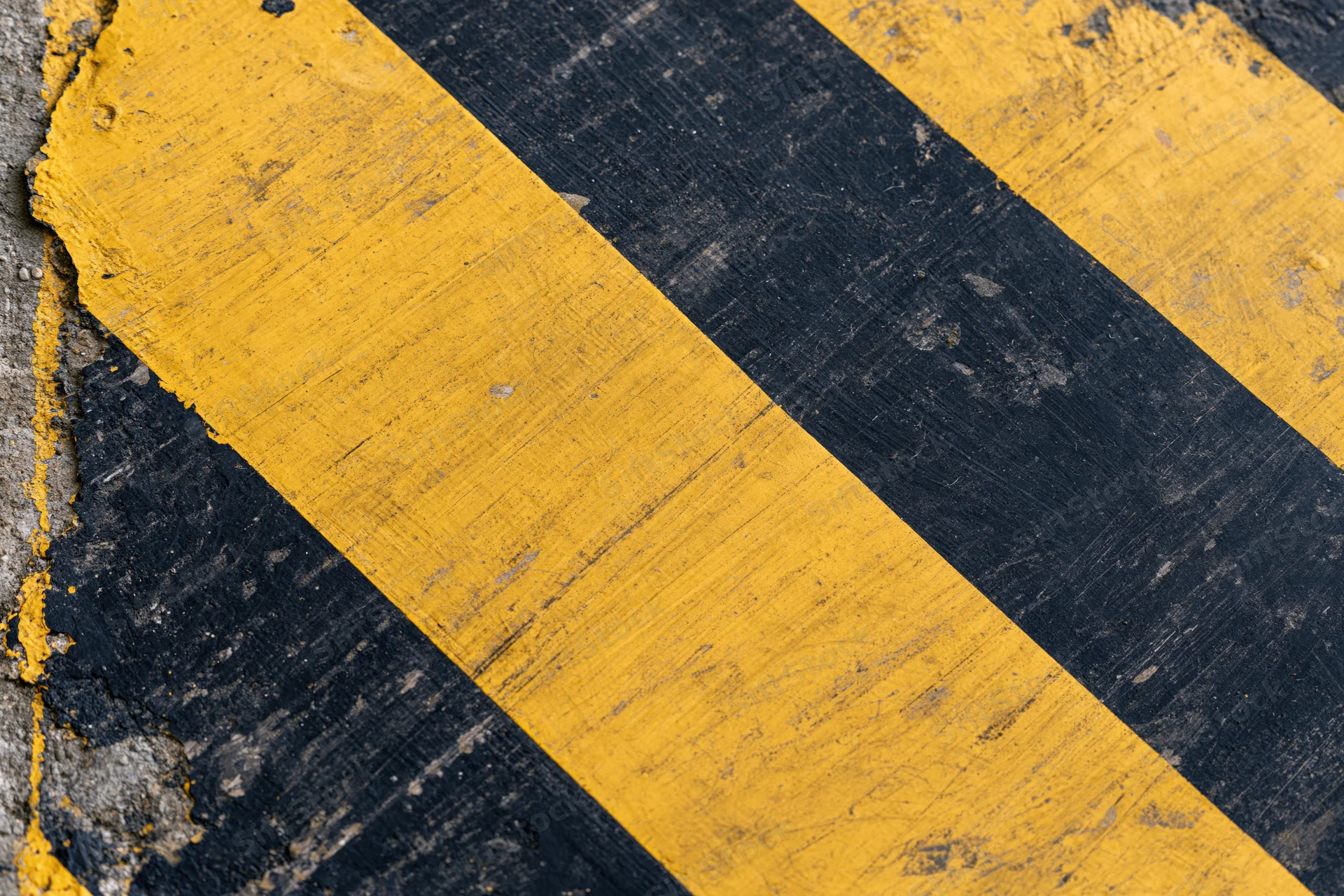 Diagonal yellow and black hazard stripes on a weathered asphalt surface