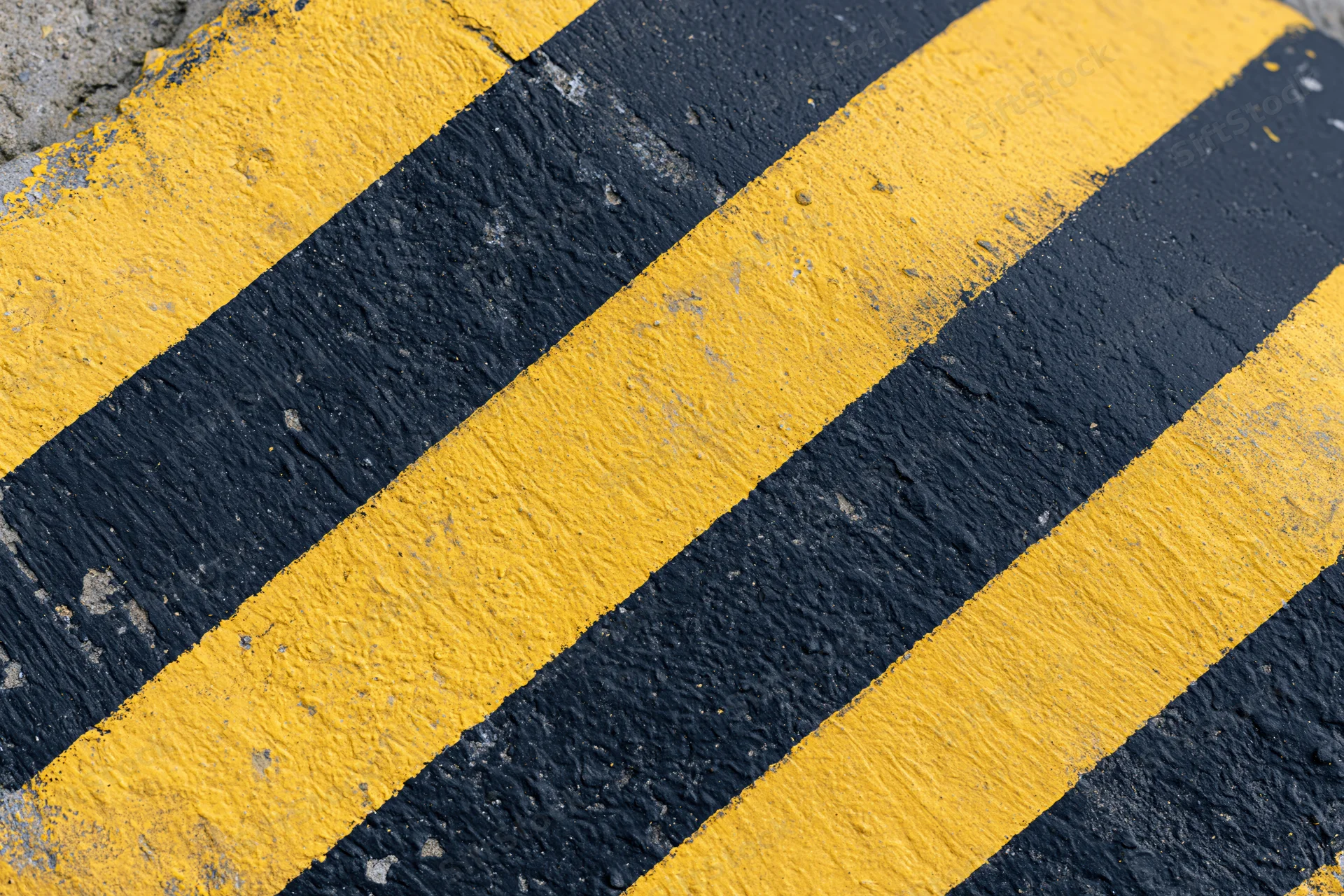 Diagonal yellow and black hazard stripes painted on a weathered concrete surface