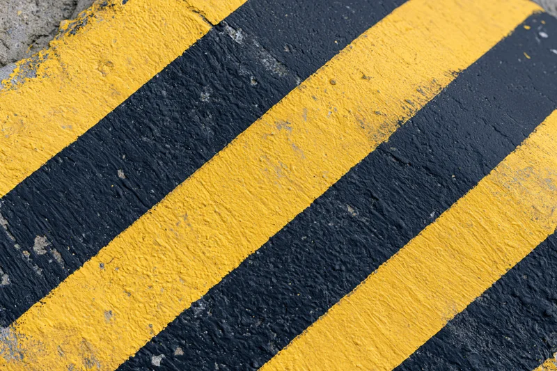 Diagonal yellow and black hazard stripes painted on a weathered concrete surface