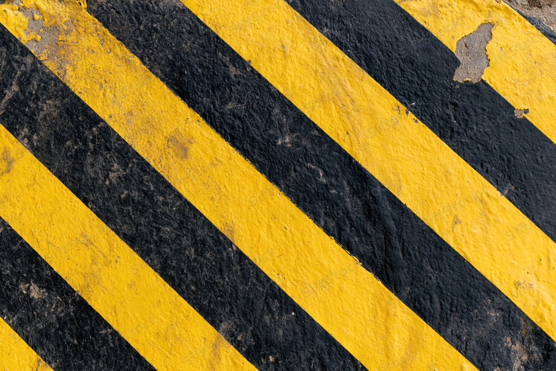 Diagonal yellow and black hazard stripes on a weathered industrial pavement surface
