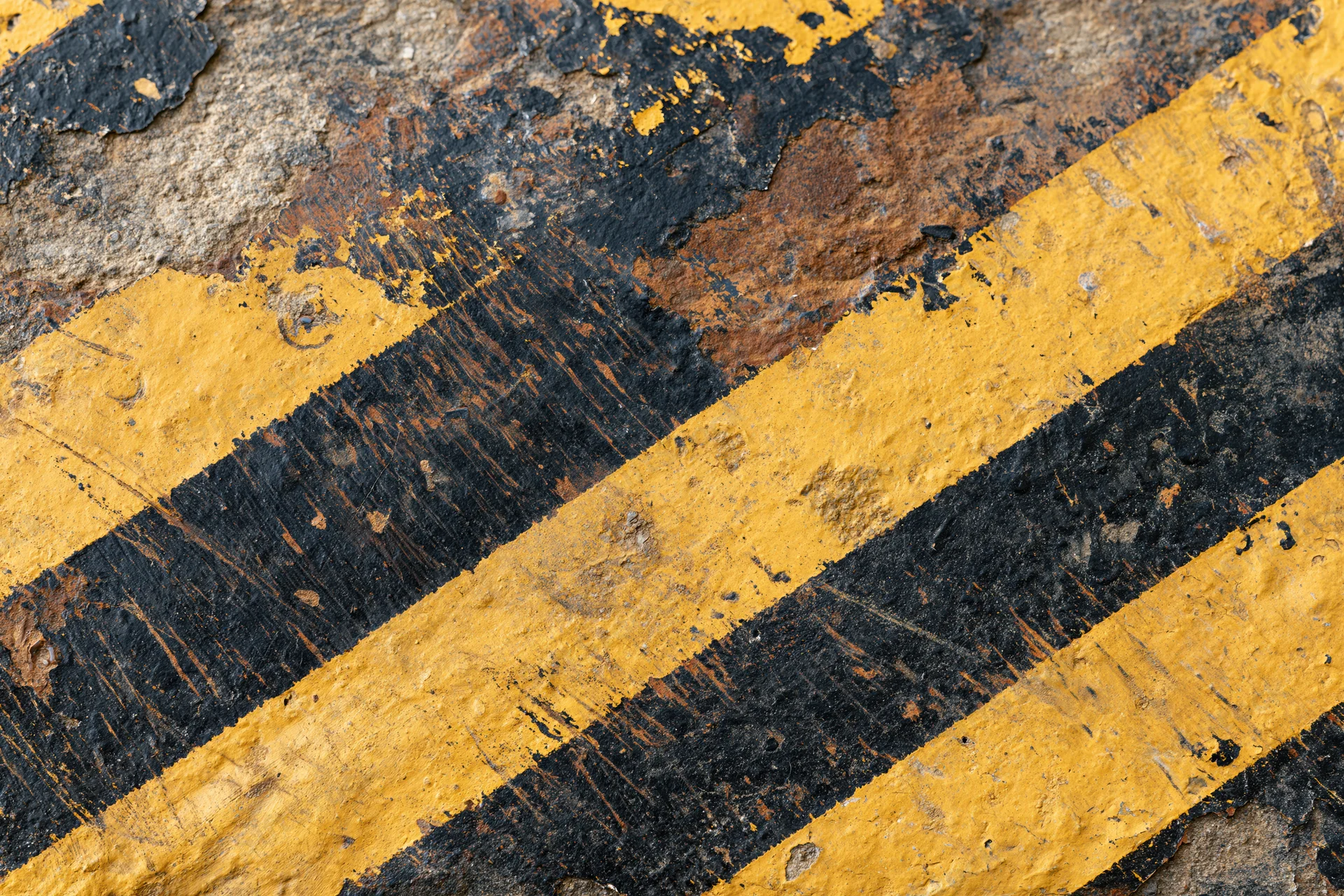 Weathered black and yellow diagonal stripes on a cracked concrete surface