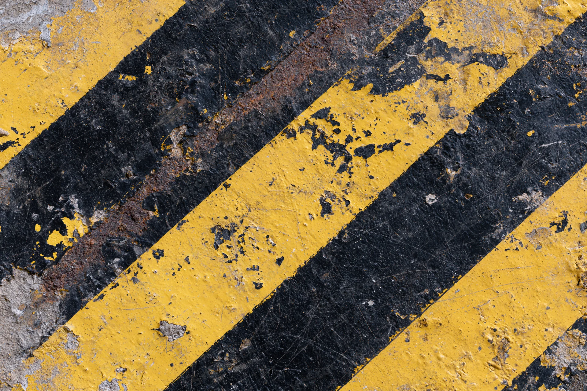 Weathered industrial warning surface with diagonal yellow and black stripes on asphalt