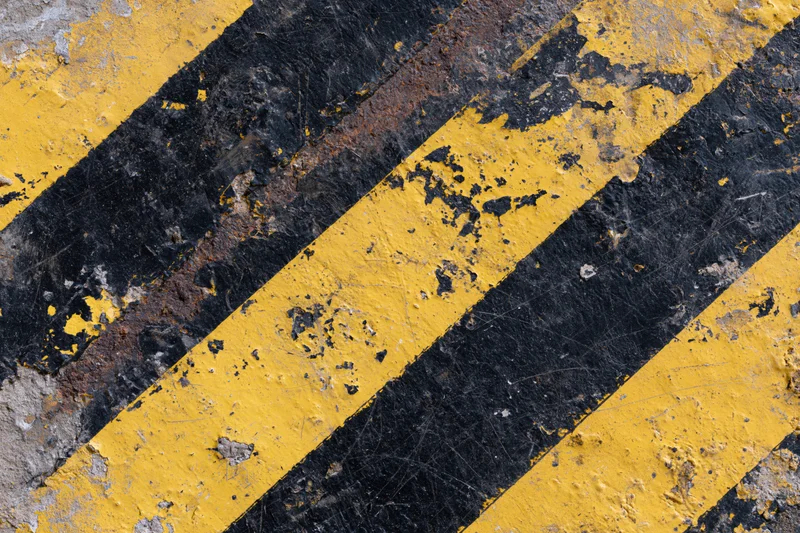 Weathered industrial warning surface with diagonal yellow and black stripes on asphalt