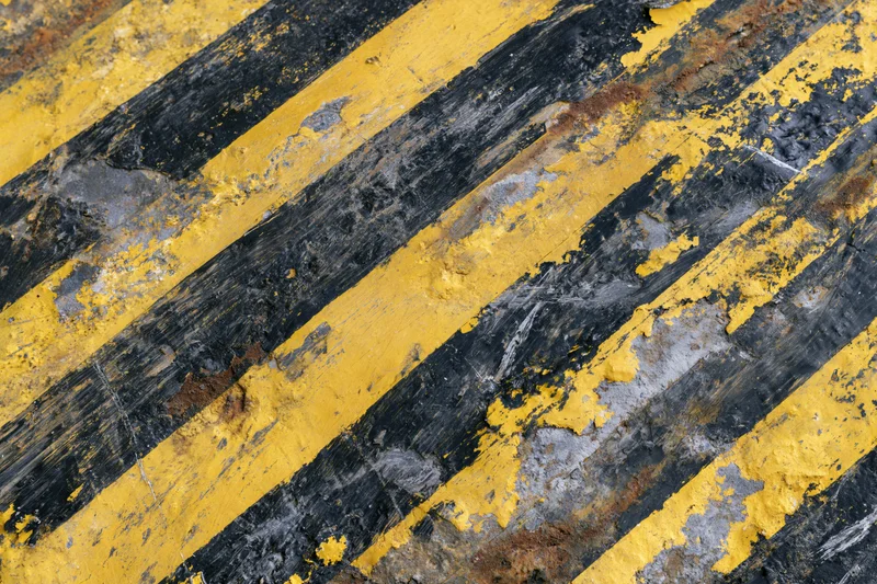 Weathered industrial warning surface with diagonal black and yellow stripes showing peeling paint and rust