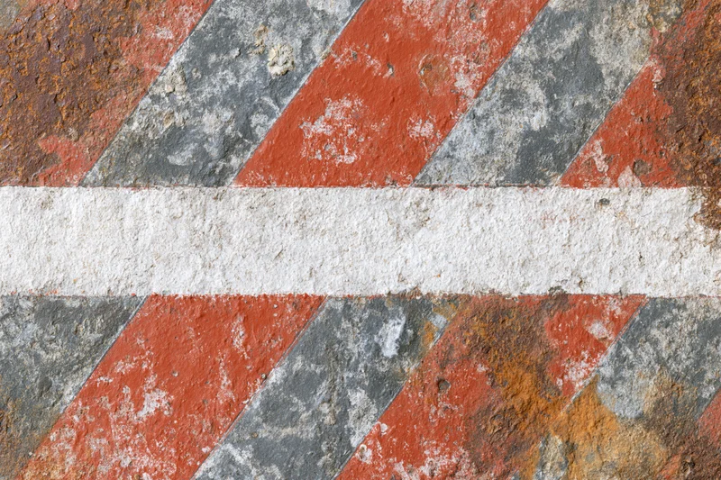 Weathered metal barrier with diagonal red and white stripes showing rust and paint wear