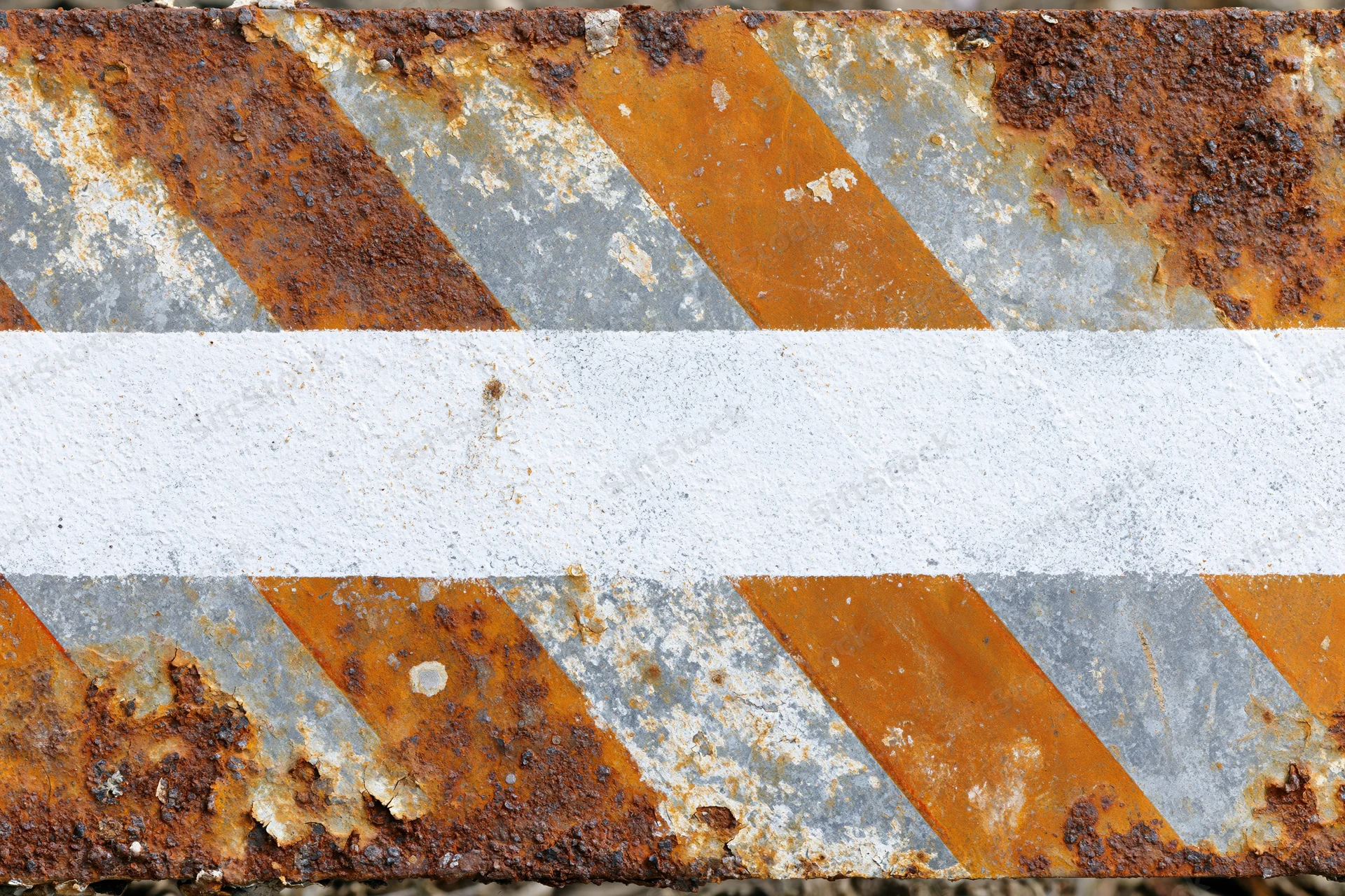 Weathered metal warning barrier with diagonal orange and white stripes showing rust and paint decay