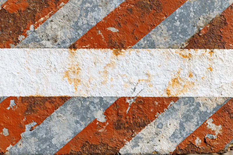 Weathered metal barrier with diagonal orange and white stripes showing rust and paint decay
