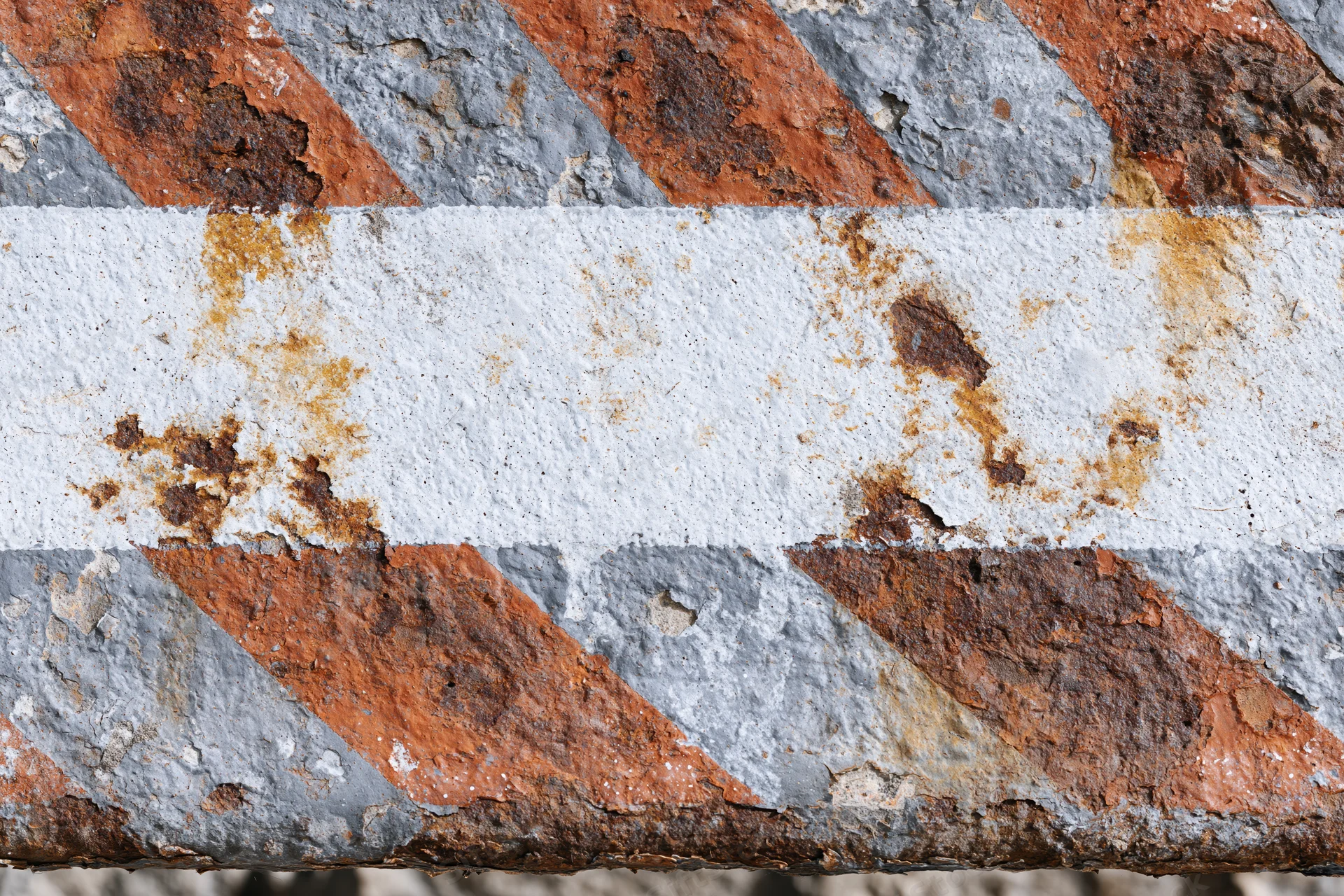 Weathered metal barrier with diagonal orange and white stripes showing rust and paint decay