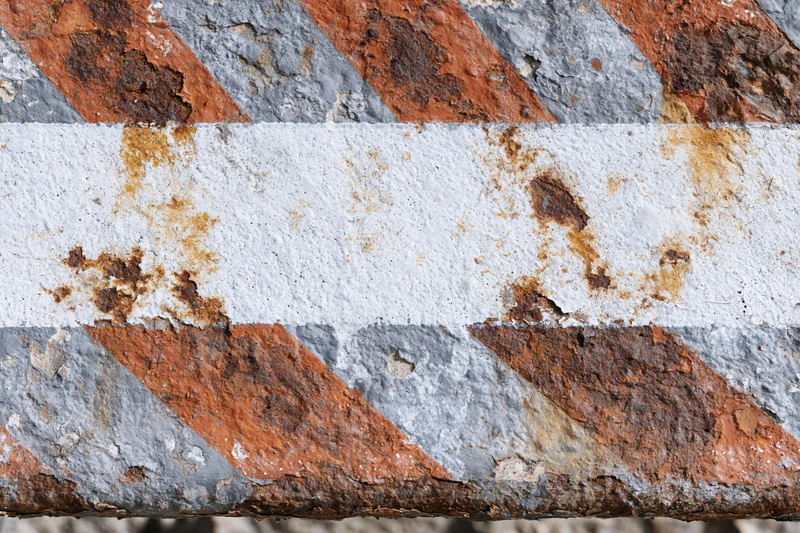 Weathered metal barrier with diagonal orange and white stripes showing rust and paint decay