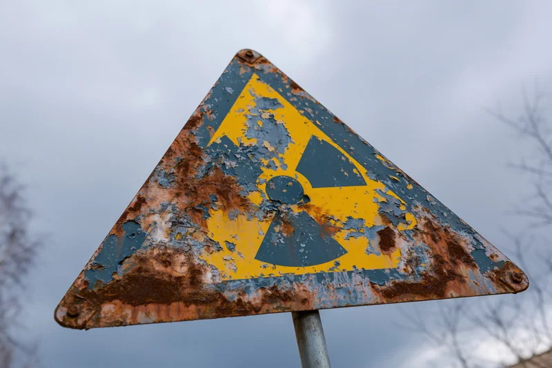 Weathered triangular radiation warning sign with peeling yellow and blue paint on a rusty metal surface outdoors under overcast sky