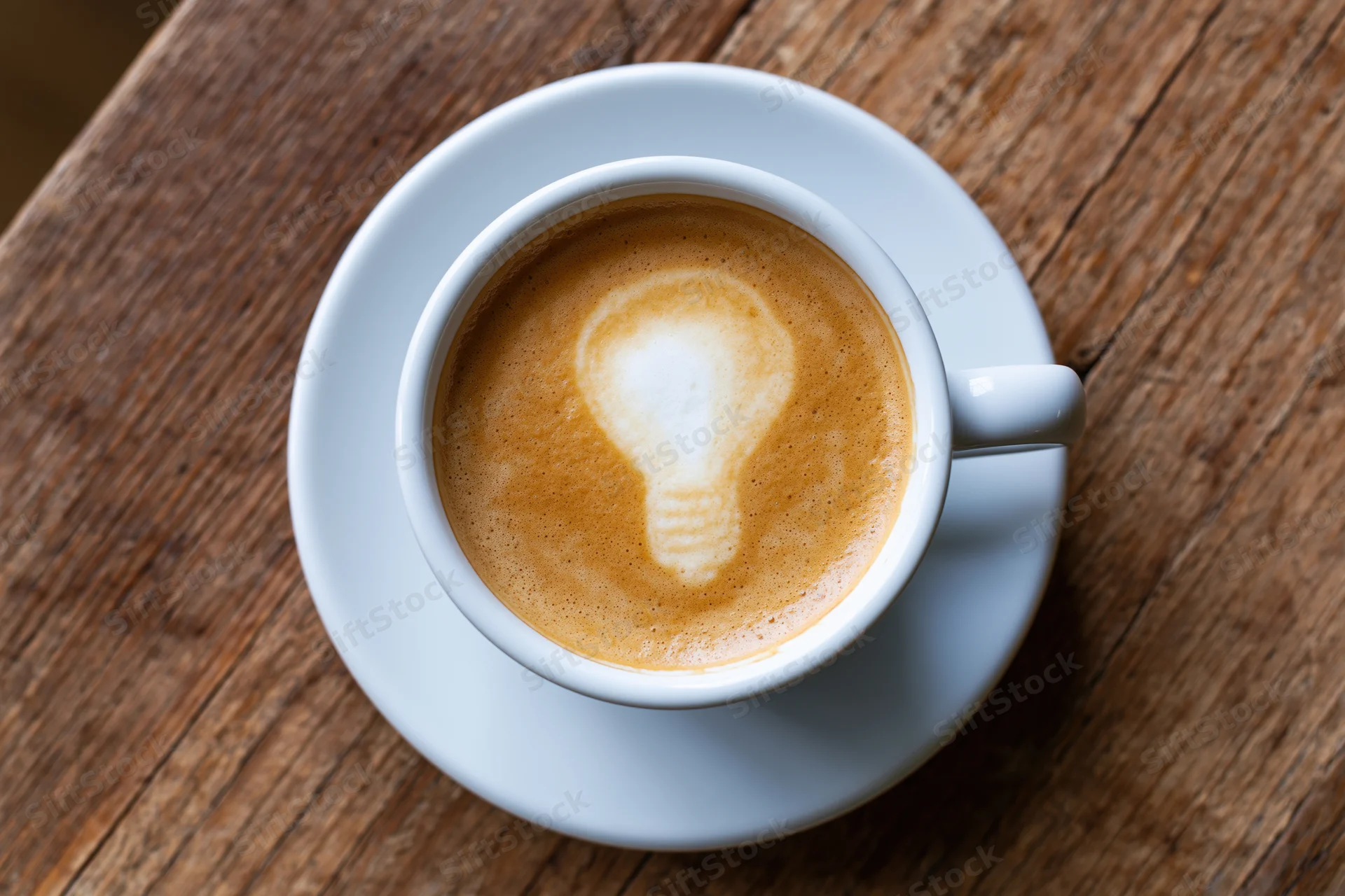 White ceramic cup of coffee with lightbulb latte art on wooden table