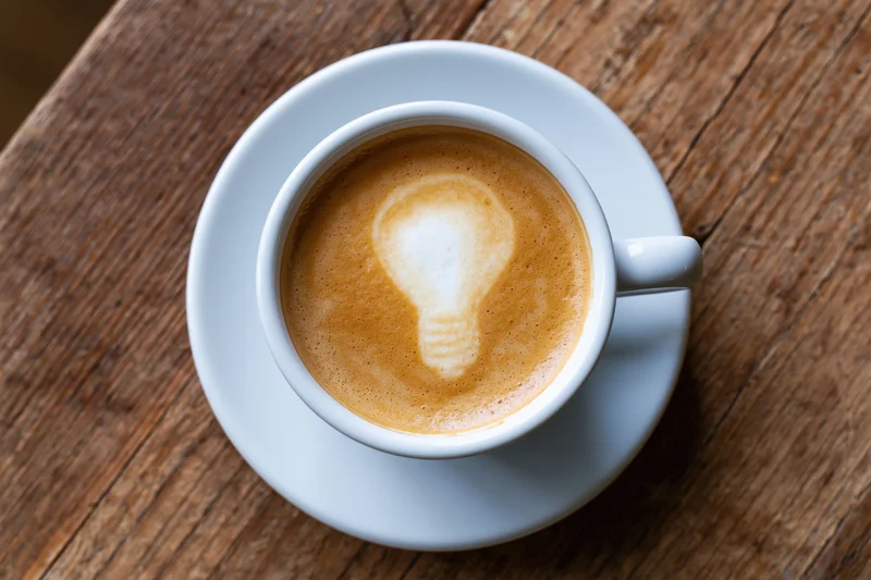 White ceramic cup of coffee with lightbulb latte art on wooden table