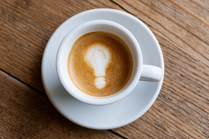 White ceramic cup of espresso with lightbulb latte art on wooden table, top view