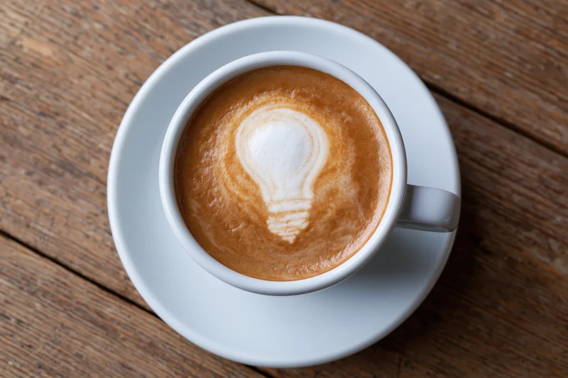White ceramic cup of coffee with lightbulb latte art on wooden table
